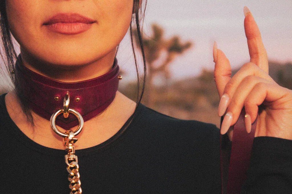 Individual wearing a Bordeaux Italian leather BDSM collar, gold chain draped over the shoulder.