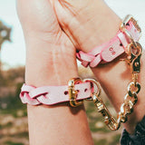 Pink leather day collar and leather wrist cuffs connected by gold chain on wrists outdoors