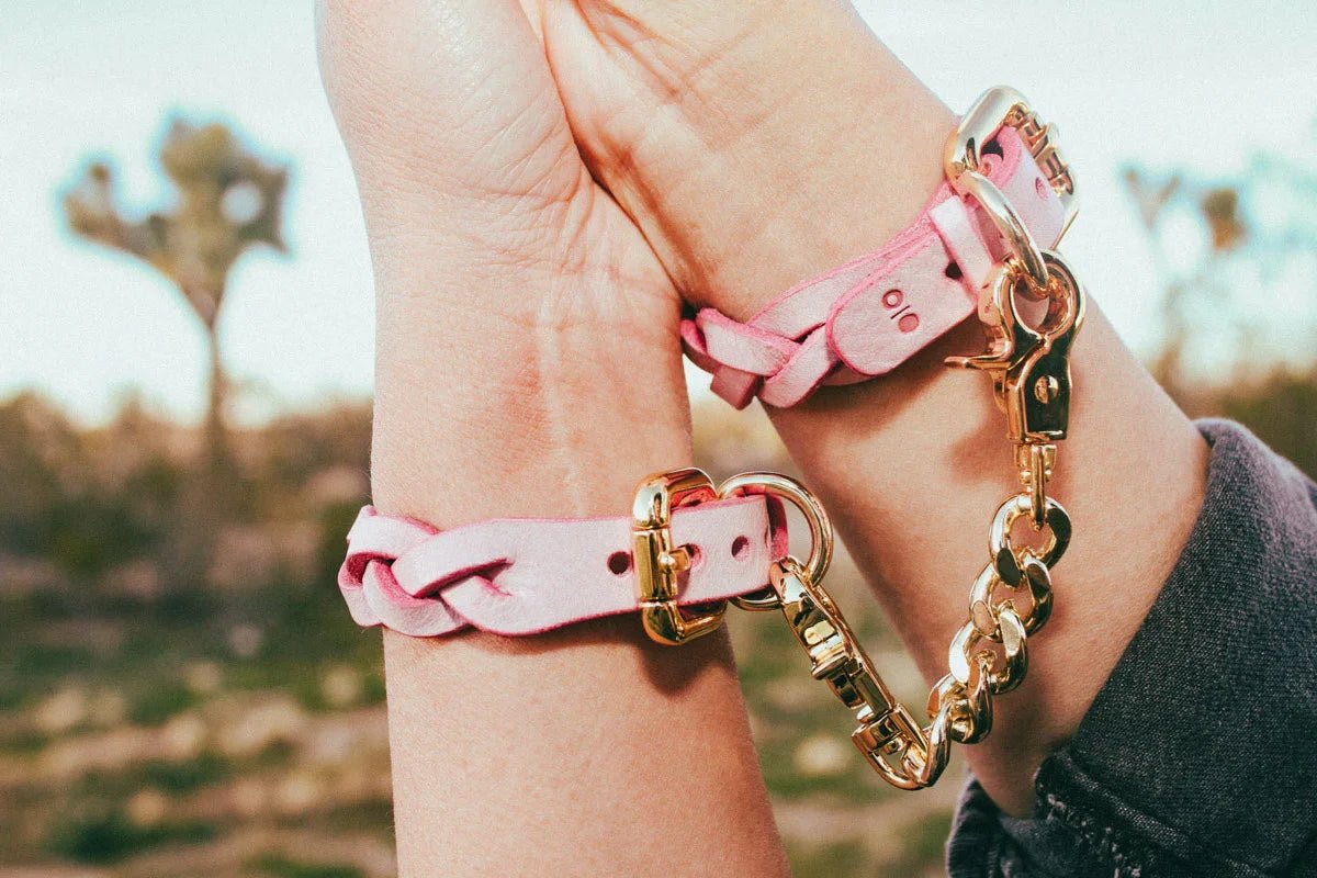 Pink leather day collar and leather wrist cuffs connected by gold chain on wrists outdoors