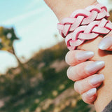 Close-up of hand wearing braided pink leather wrist cuffs outdoors with natural background