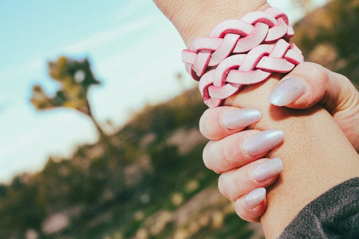 Close-up of hand wearing braided pink leather wrist cuffs outdoors with natural background