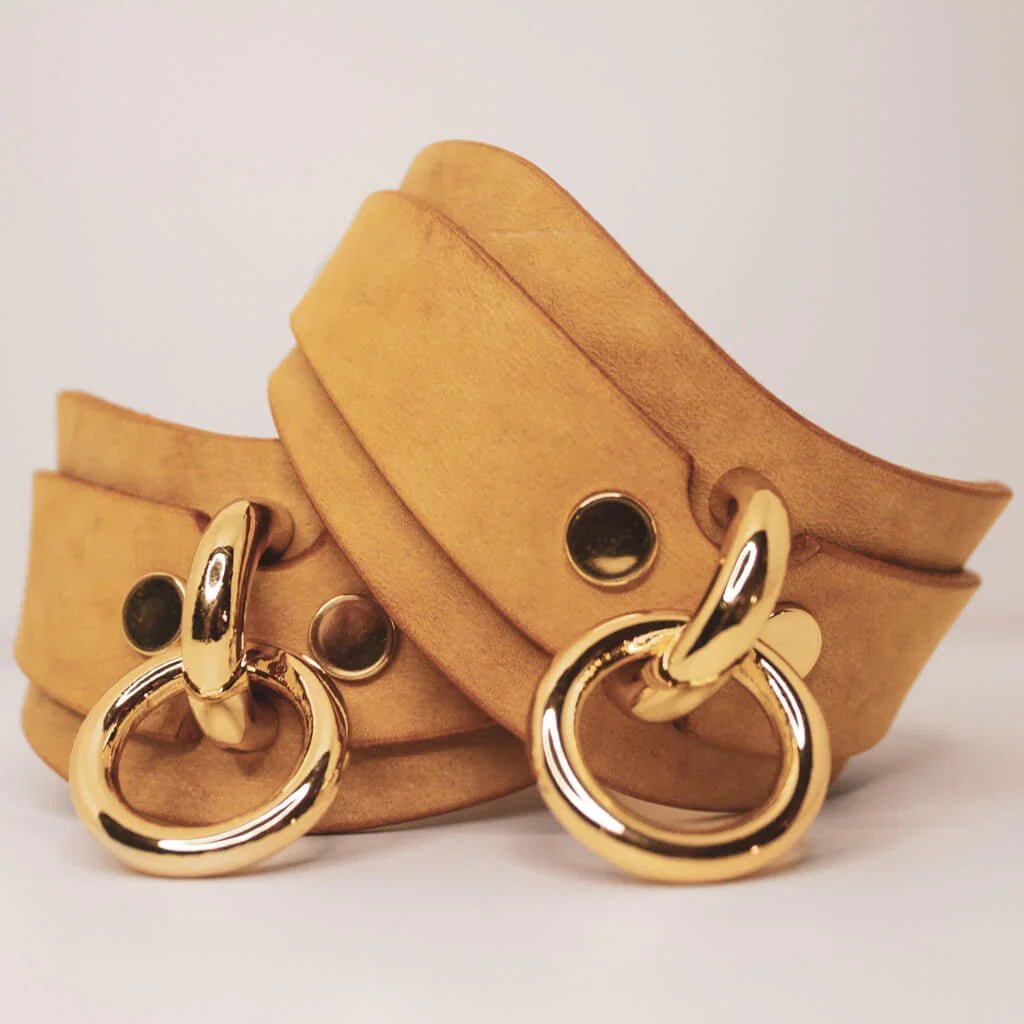Golden Hour suede BDSM cuffs with gold-tone O-rings and hardware, piled elegantly.