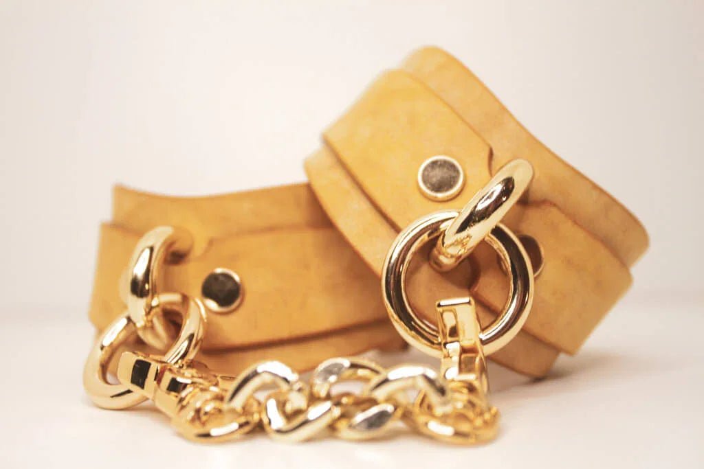 Stacked Golden Hour leather BDSM cuffs with gold-tone details on a neutral background.