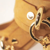 Pair of Golden Hour Italian leather BDSM cuffs with gold-tone chain laid out side by side.