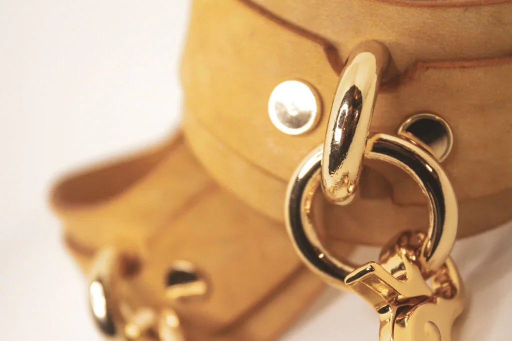 Pair of Golden Hour Italian leather BDSM cuffs with gold-tone chain laid out side by side.