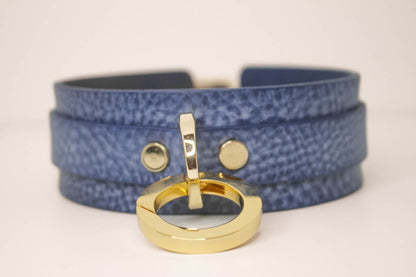 Lifestyle shot of a person wearing a denim leather BDSM collar, showcasing its fit and the gold-tone O-ring detail, set against a natural outdoor backdrop.