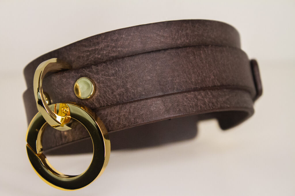 Angled perspective of the 'Mesa' brown leather BDSM collar showing off the wraparound leather strap and elegant gold-tone O-ring centerpiece.