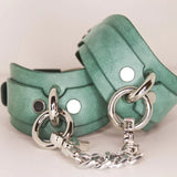 Elegantly crafted teal Italian leather BDSM cuffs with silver hardware, set against a white background.