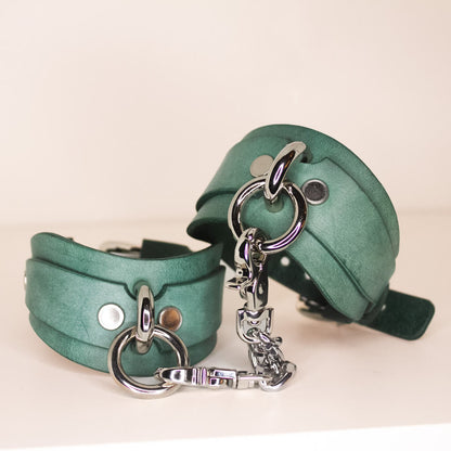 Close-up of a stack of teal handmade Italian leather cuffs with luxury silver-tone buckles and rivets.