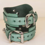 Back detail of two handmade teal Italian leather cuffs connected by a silver chain, showcasing luxury and kink.