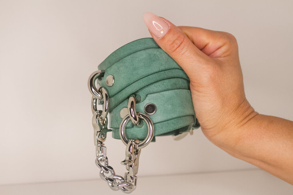 Hand holding a teal Italian leather cuff linked with a silver chain, showcasing handmade luxury.