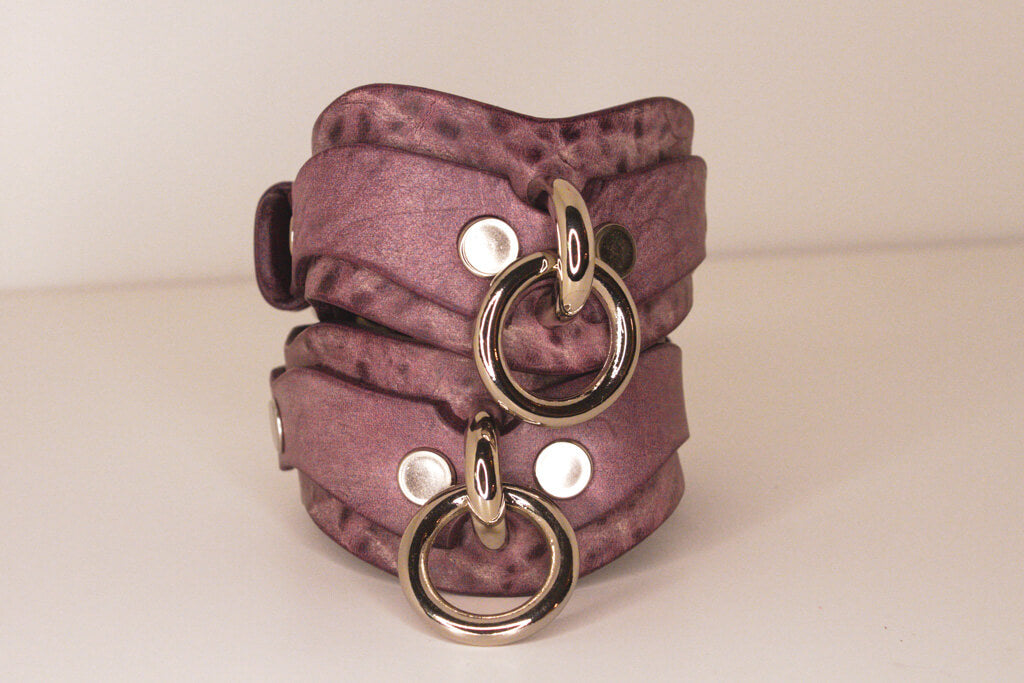 Stack of Haze purple leather BDSM cuffs with silver-tone O-rings and buckles.