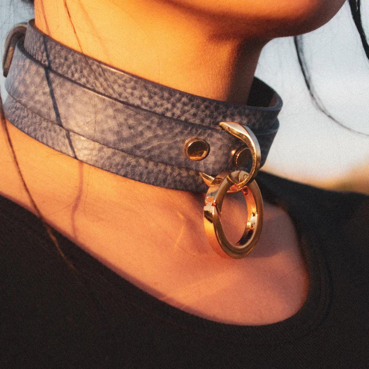 Close-up of a person's neck wearing a textured gray leather day collar with a large gold ring detail