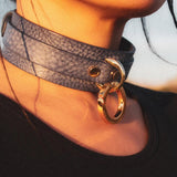 Close-up of a person's neck wearing a textured gray leather day collar with a large gold ring detail
