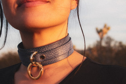 Close-up lifestyle image of a person wearing a denim leather BDSM collar, emphasizing the collar's texture and O-ring detail, with soft-focus background for an artistic effect.