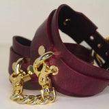 Stacked Bordeaux leather BDSM cuffs with gold-tone buckle closures, gold chains and rivet details.