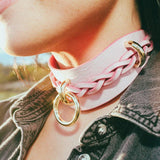Close-up of a person wearing a pink leather day collar with braided detail and gold rings, styled with a denim jacket