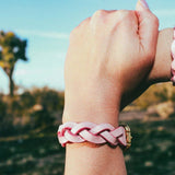 Wrist wearing pink braided leather wrist cuffs outdoors with blurred natural background