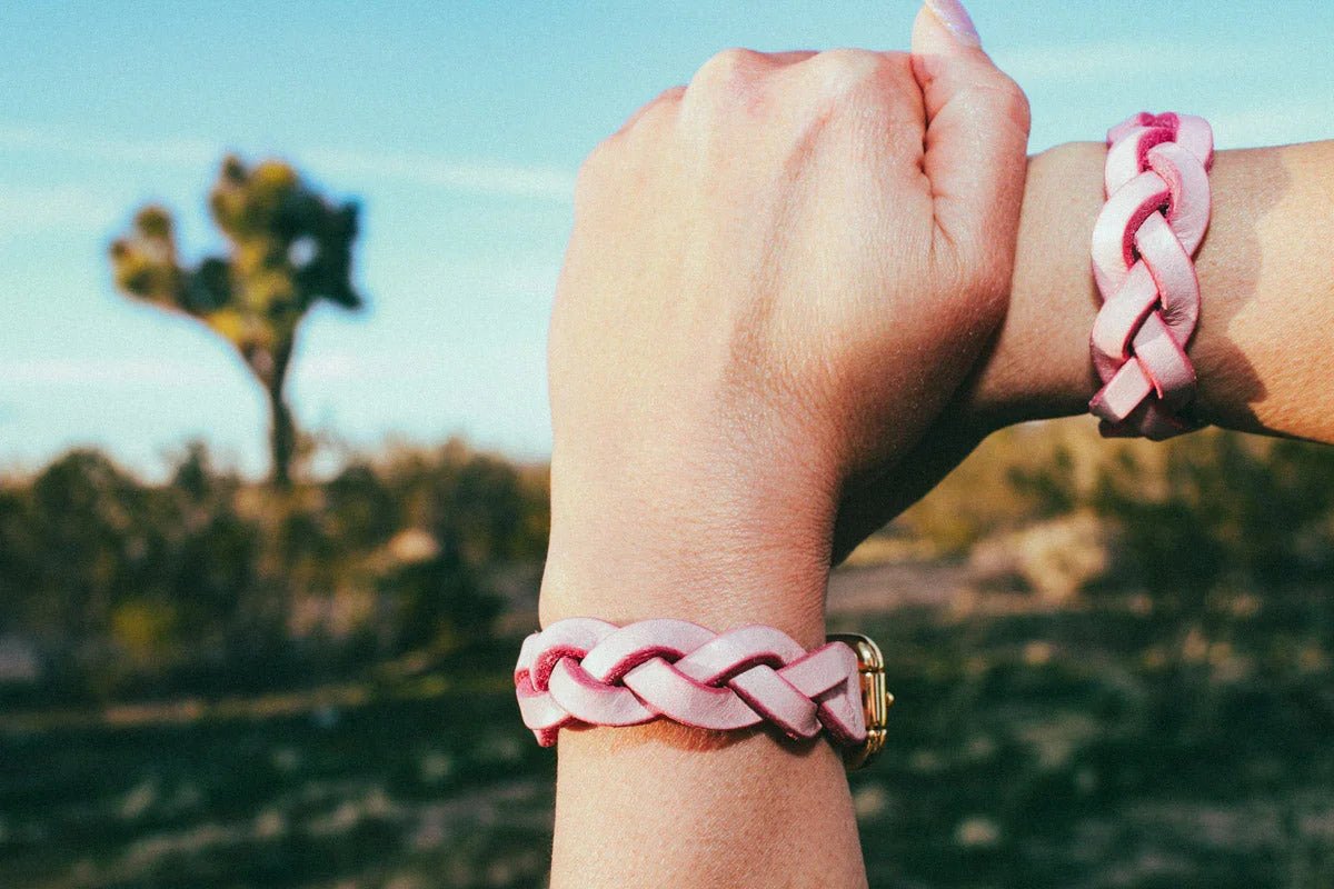 Wrist wearing pink braided leather wrist cuffs outdoors with blurred natural background
