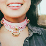 Close-up of smiling person wearing pink leather day collar with gold hardware outdoors