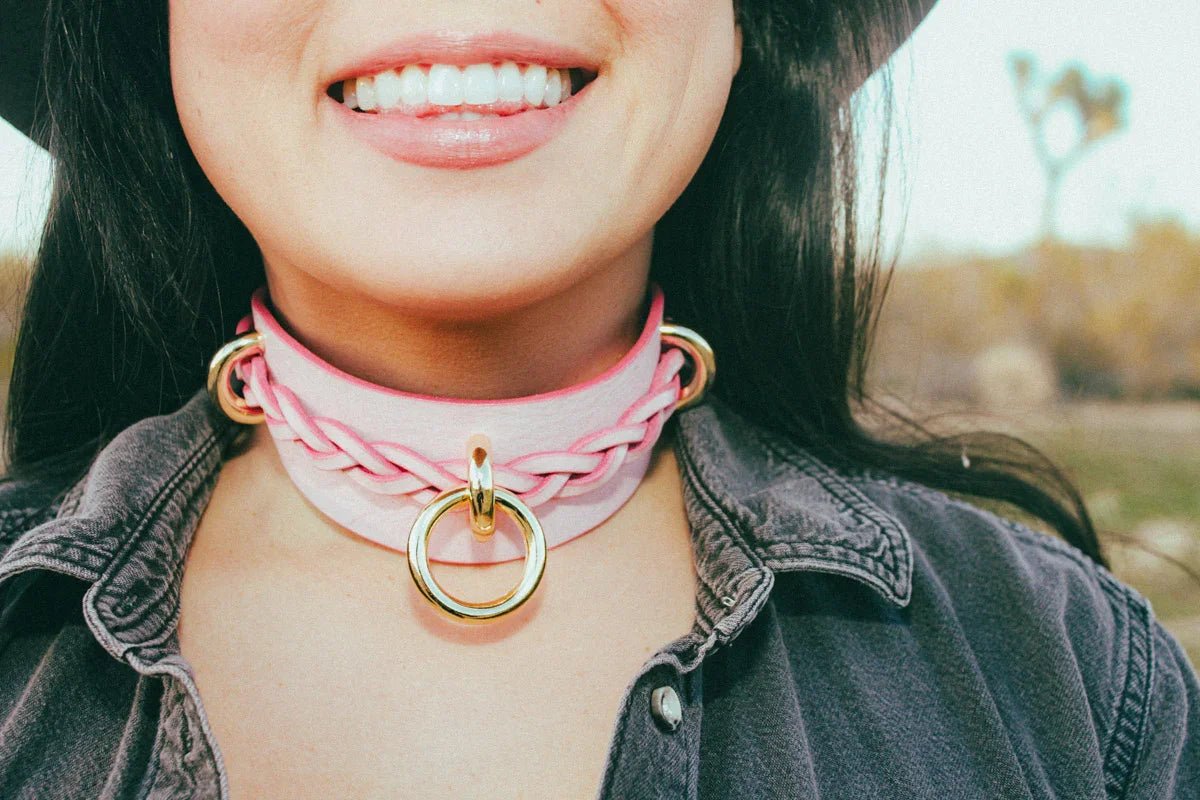 Close-up of smiling person wearing pink leather day collar with gold hardware outdoors