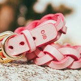 Pink braided leather wrist cuffs with gold-tone buckle and ring resting on a textured stone surface