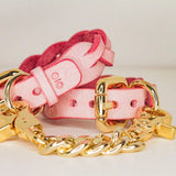 Pink leather wrist cuffs with gold buckles and chain detail on white background
