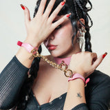 Person wearing pink leather day collar and matching leather wrist cuffs connected by gold chain
