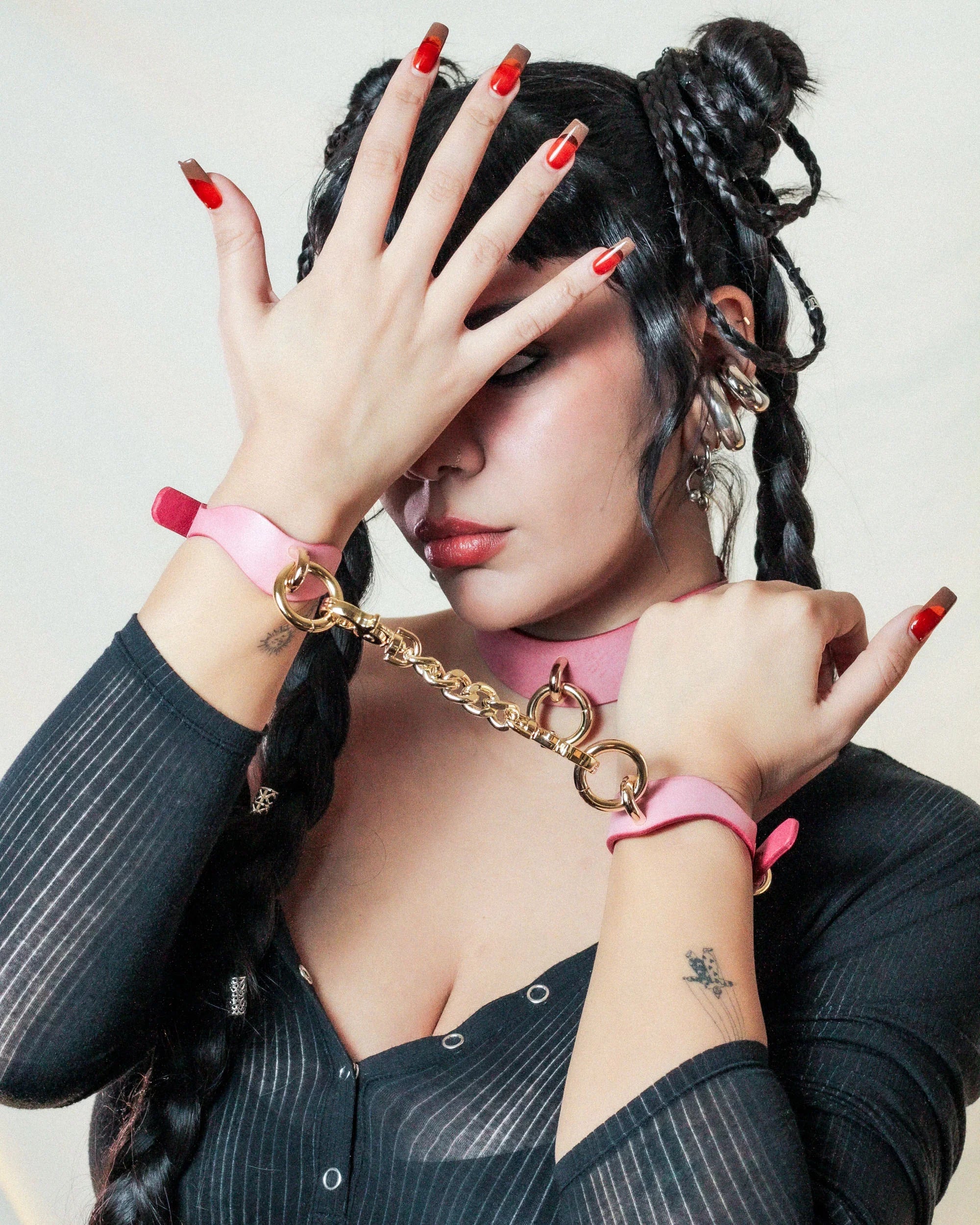 Person wearing pink leather day collar and matching leather wrist cuffs connected by gold chain