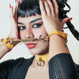 Woman wearing yellow leather day collar and matching leather wrist cuffs connected by a gold chain