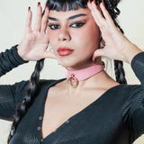 Woman wearing a pink leather day collar with a gold ring, styled with black top and braided hair