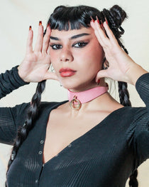 Woman wearing a pink leather day collar with a gold ring, styled with black top and braided hair