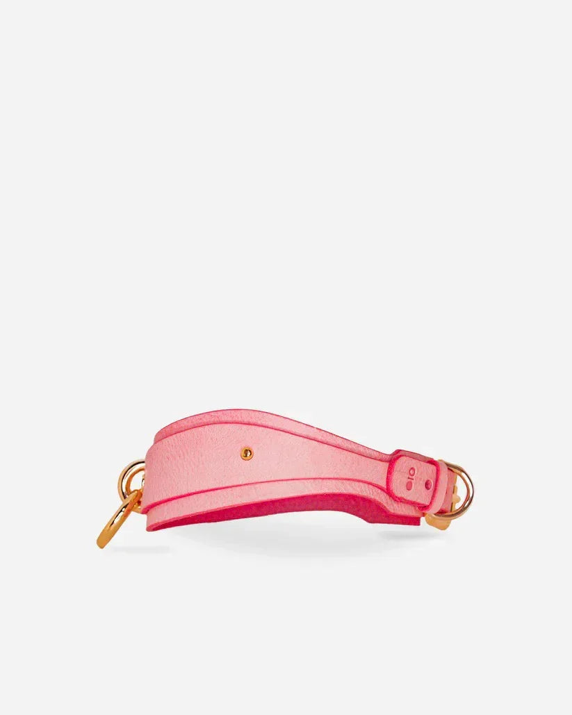 Pink leather wrist cuff with gold hardware, minimalist design, and sturdy buckle closure