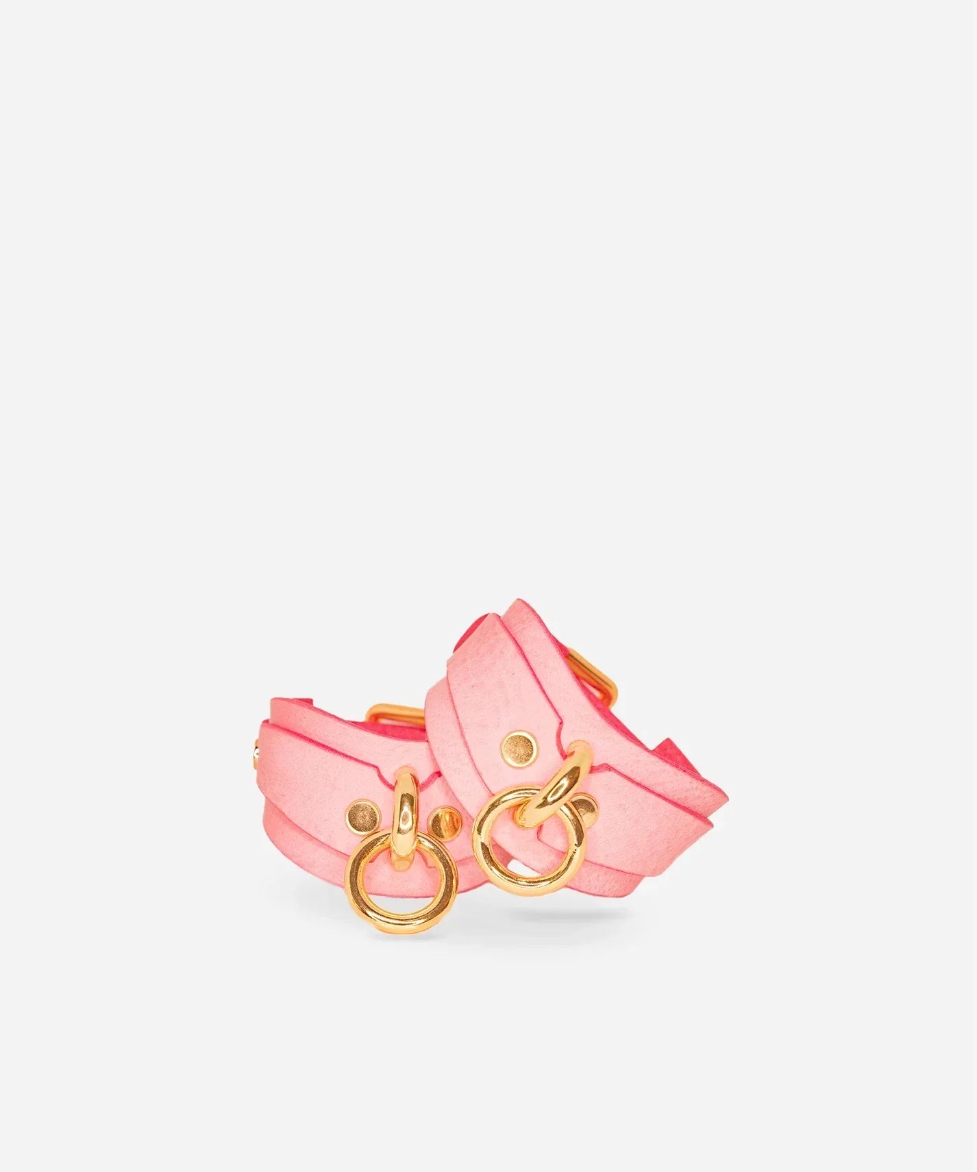 Pair of pink leather wrist cuffs with gold-tone O-rings and rivets on white background