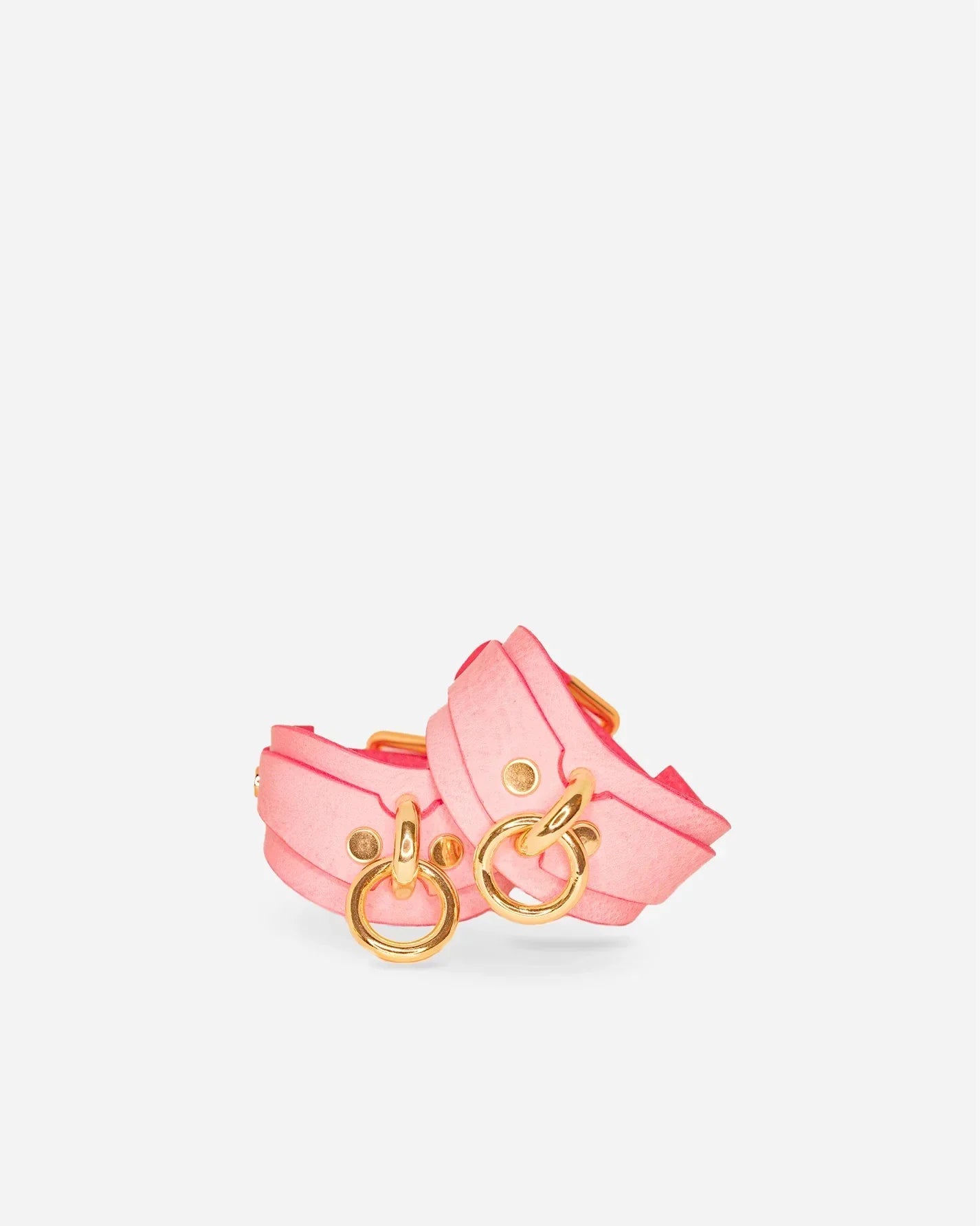 Pair of pink leather wrist cuffs with gold-tone O-rings and rivets on white background