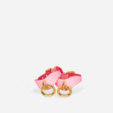 Pair of pink leather wrist cuffs with gold rings on white background, leather collars accessory