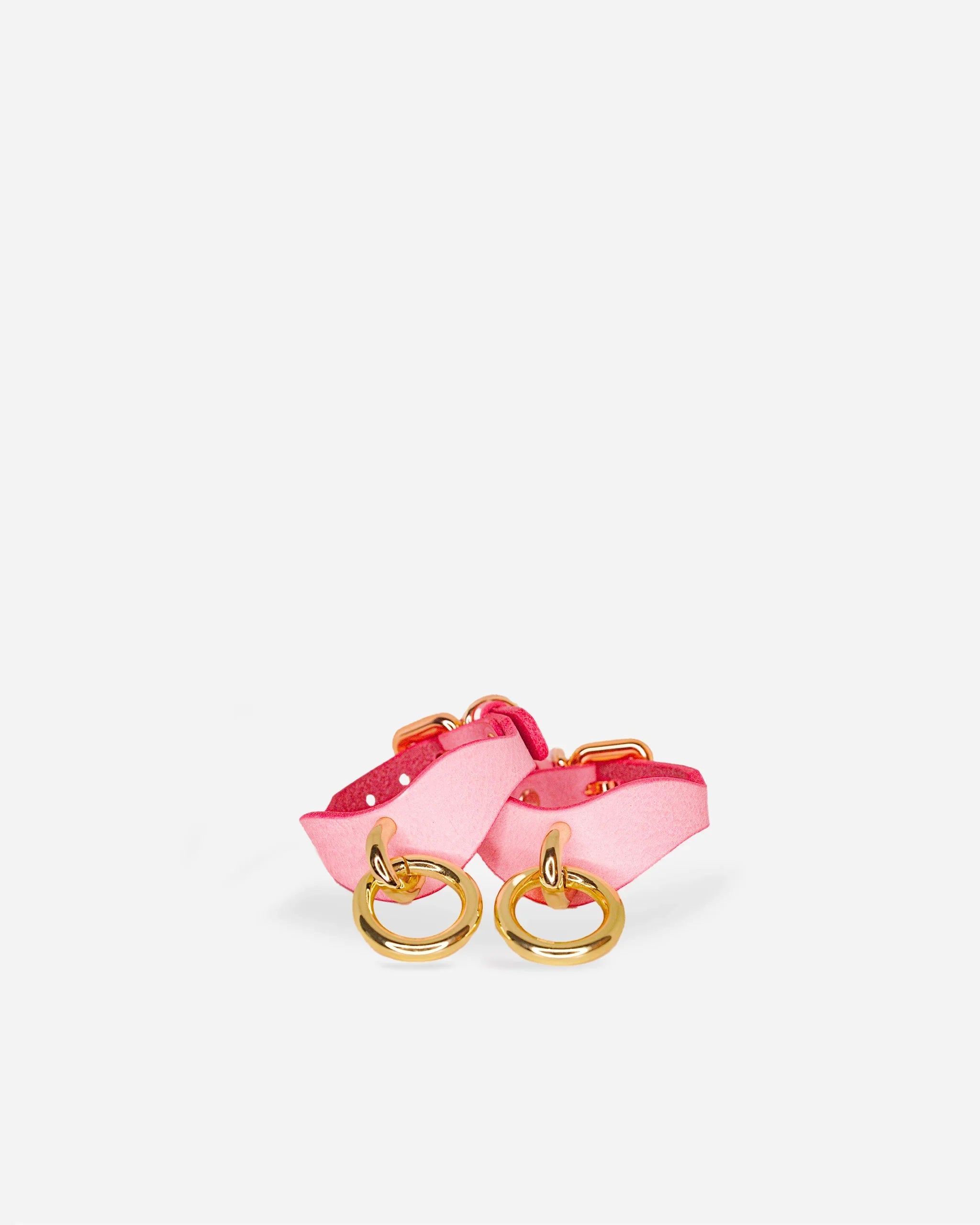Pair of pink leather wrist cuffs with gold rings on white background, leather collars accessory