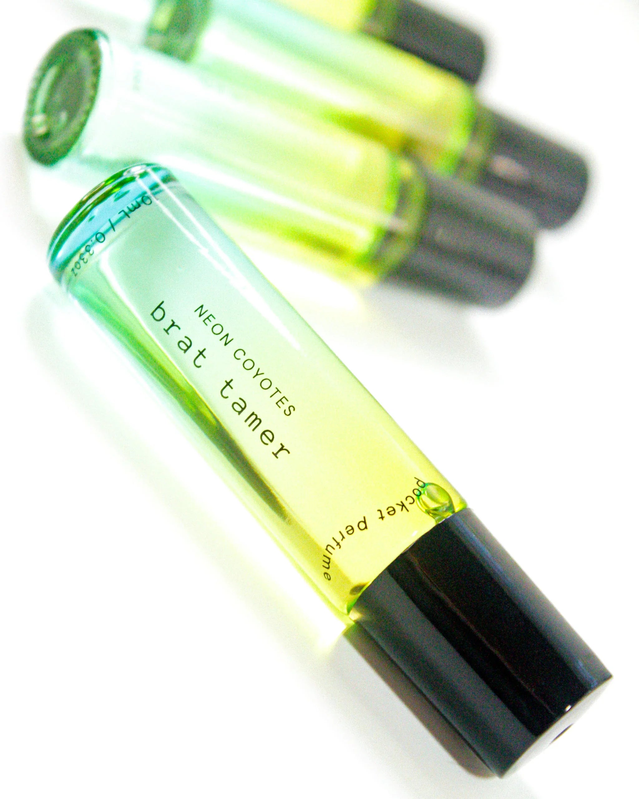 Neon Coyotes brat tamer pocket perfume vial with black cap, part of collection including three yellow-green glass bottles