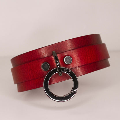 Elegant 'Blood Moon' red leather BDSM collar with a striking black O-ring centerpiece and matching black rivets, presented on a clean white background.