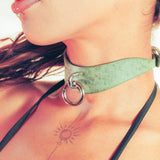 Close-up of a woman wearing a green leather day collar with metal rings.