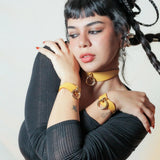 Woman with black braided hair wearing mustard yellow leather day collar and leather wrist cuffs with gold rings
