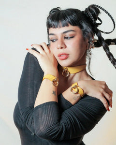 Woman with black braided hair wearing mustard yellow leather day collar and leather wrist cuffs with gold rings