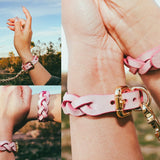 Pink leather wrist cuffs and braided leather day collar connected by gold chain outdoors