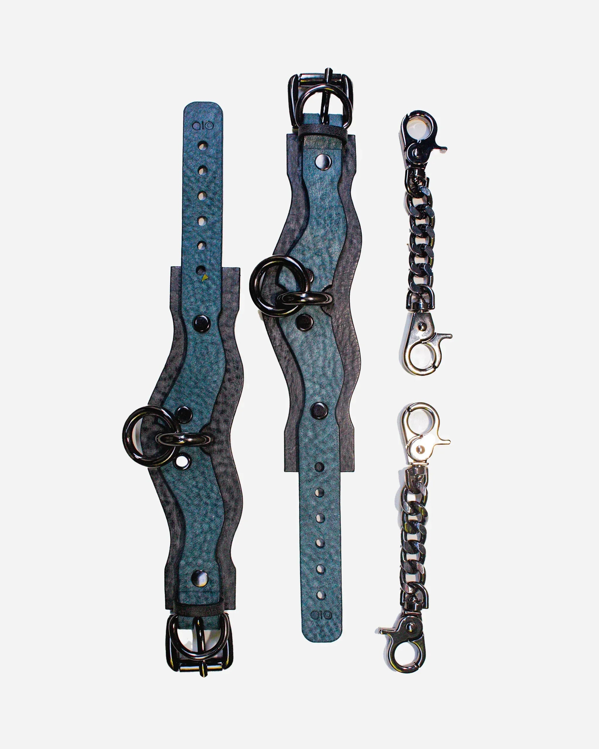 Overhead view of custom Italian leather cuffs with black hardware and metal chain connectors on white background