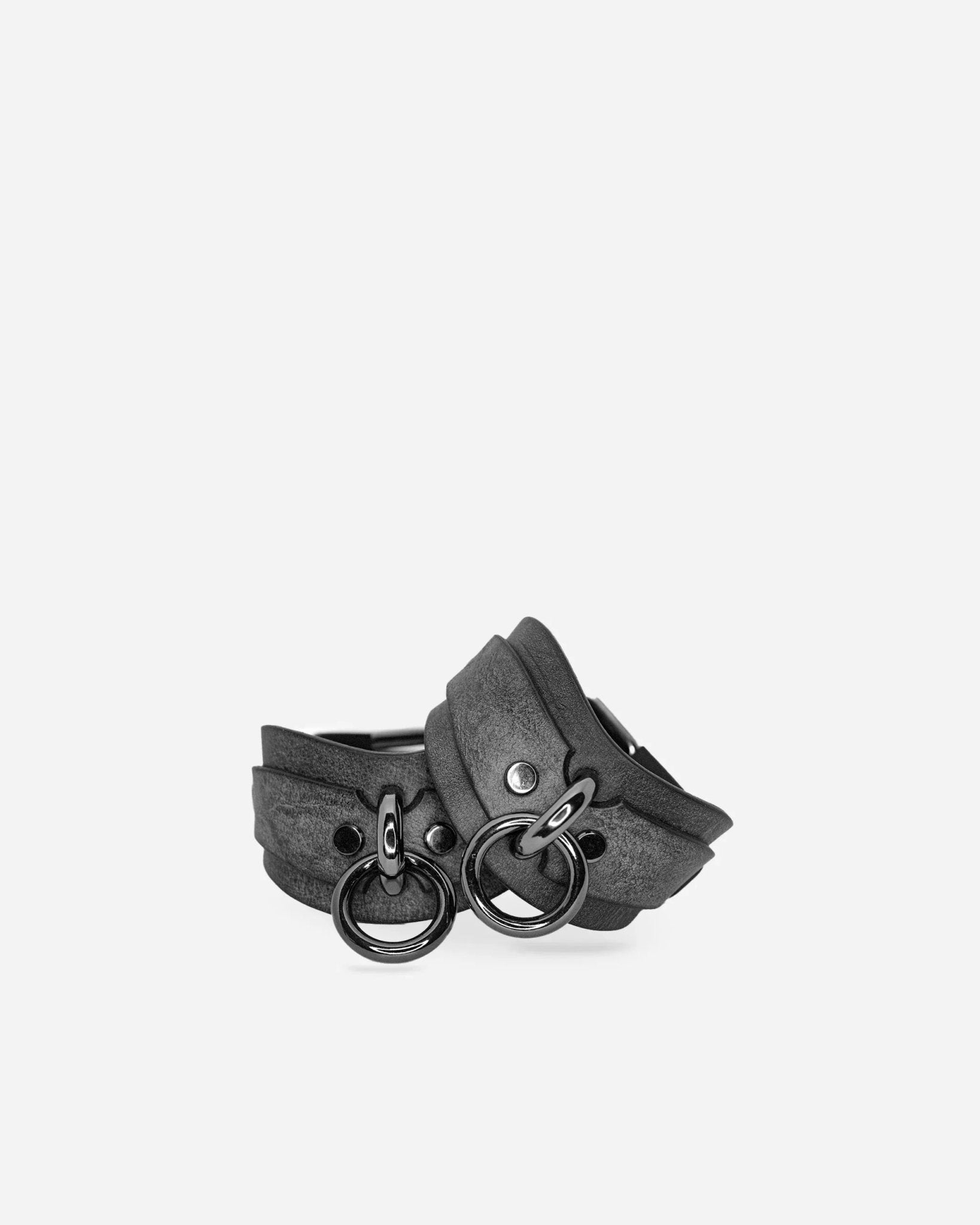 Pair of dark leather wrist cuffs with metal rings, black hardware on plain background