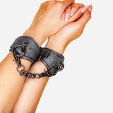 Hands wearing black leather wrist cuffs with chain connection on white background