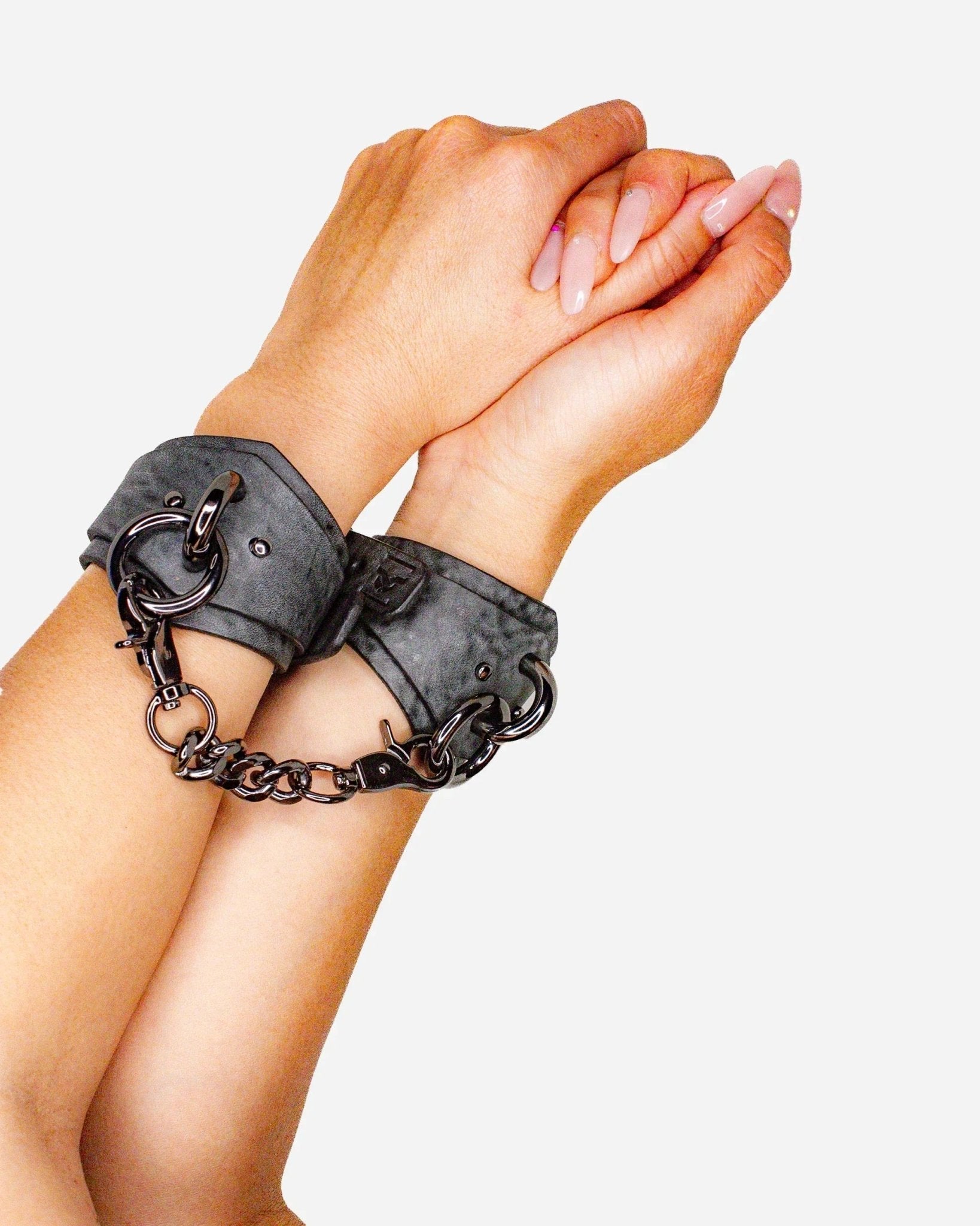 Hands wearing black leather wrist cuffs with chain connection on white background