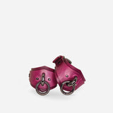 Pair of burgundy leather wrist cuffs with black metal rings and rivets on white background