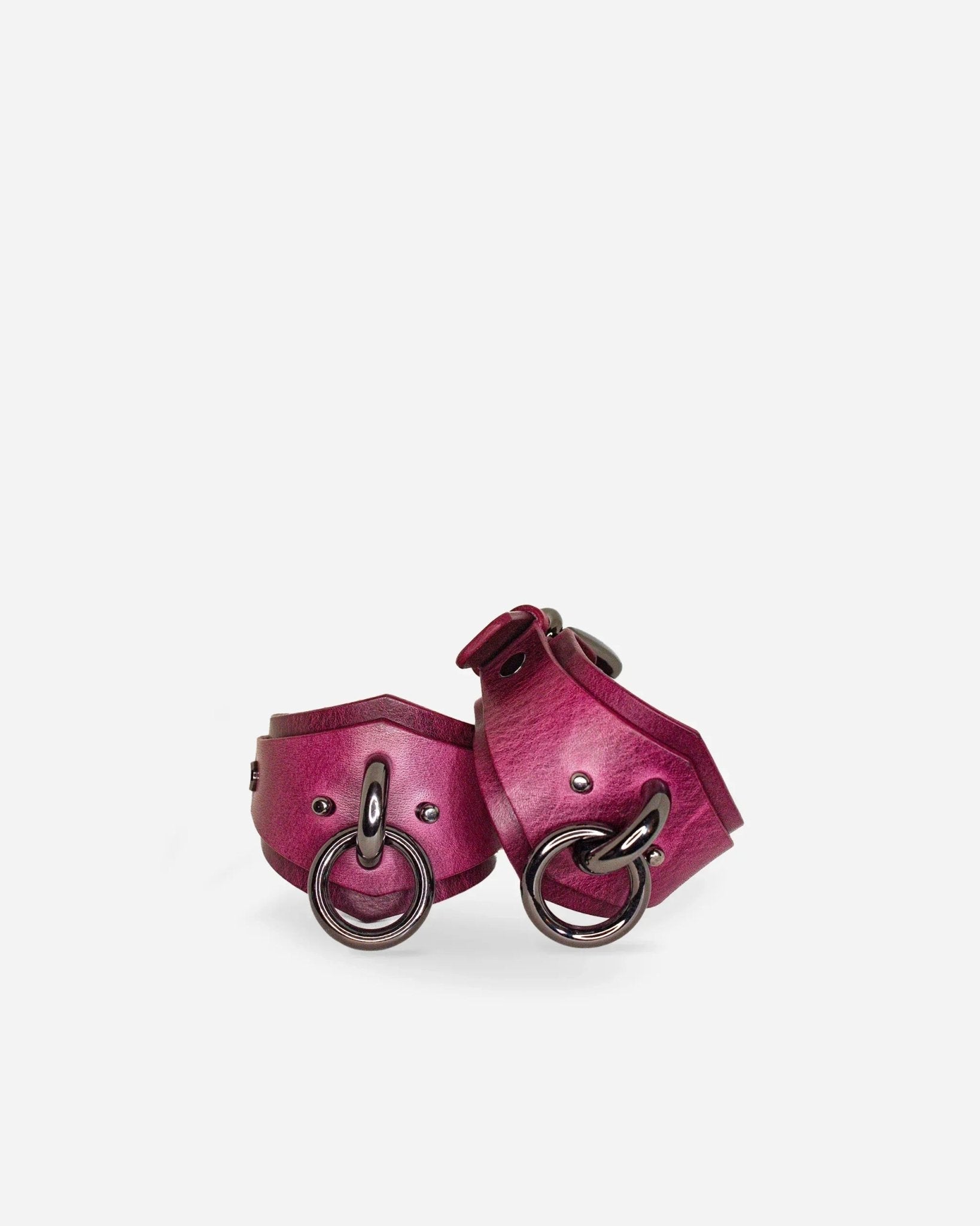 Pair of burgundy leather wrist cuffs with black metal rings and rivets on white background