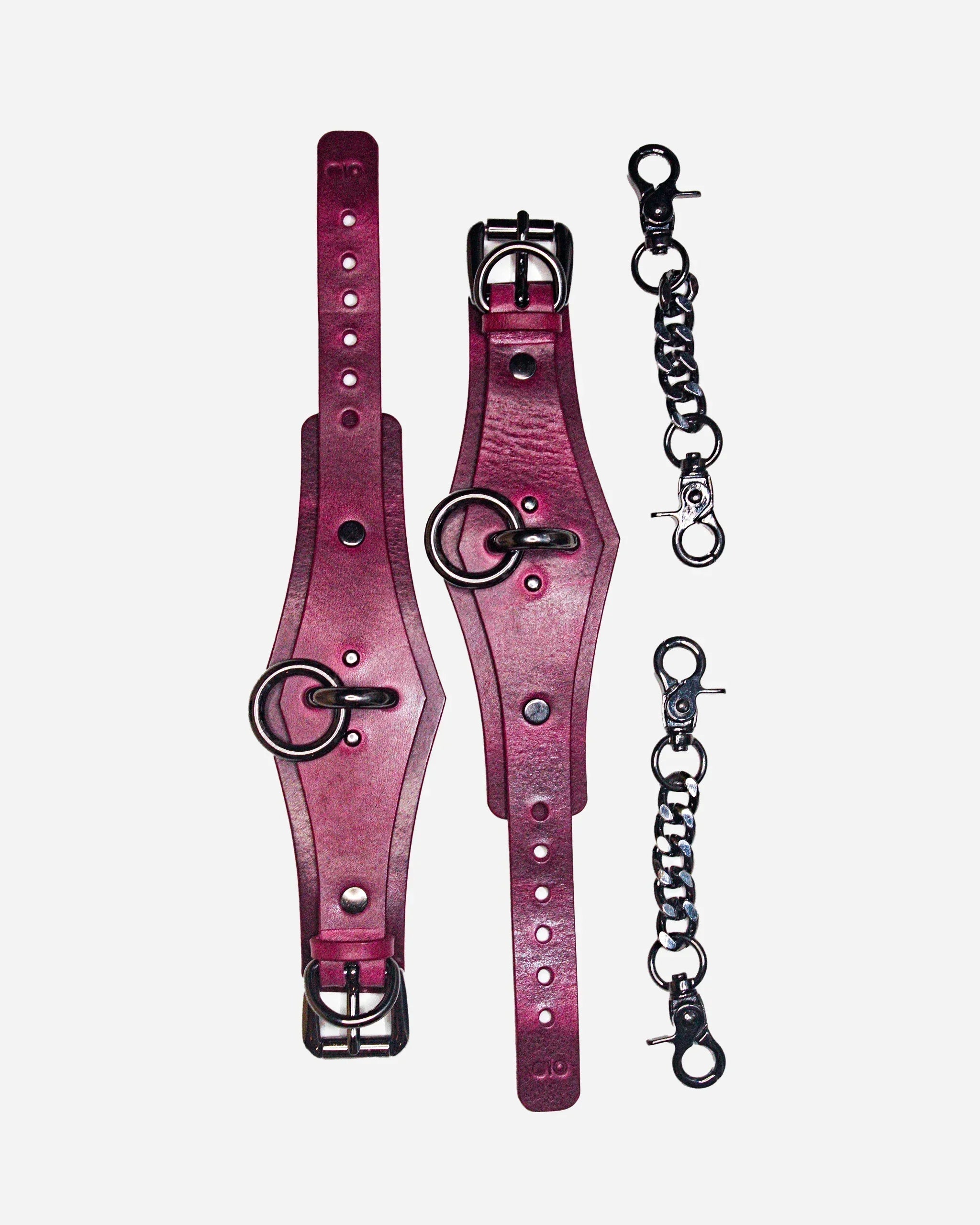 Overhead view of burgundy leather cuffs with metal rings and detachable silver chains on white background